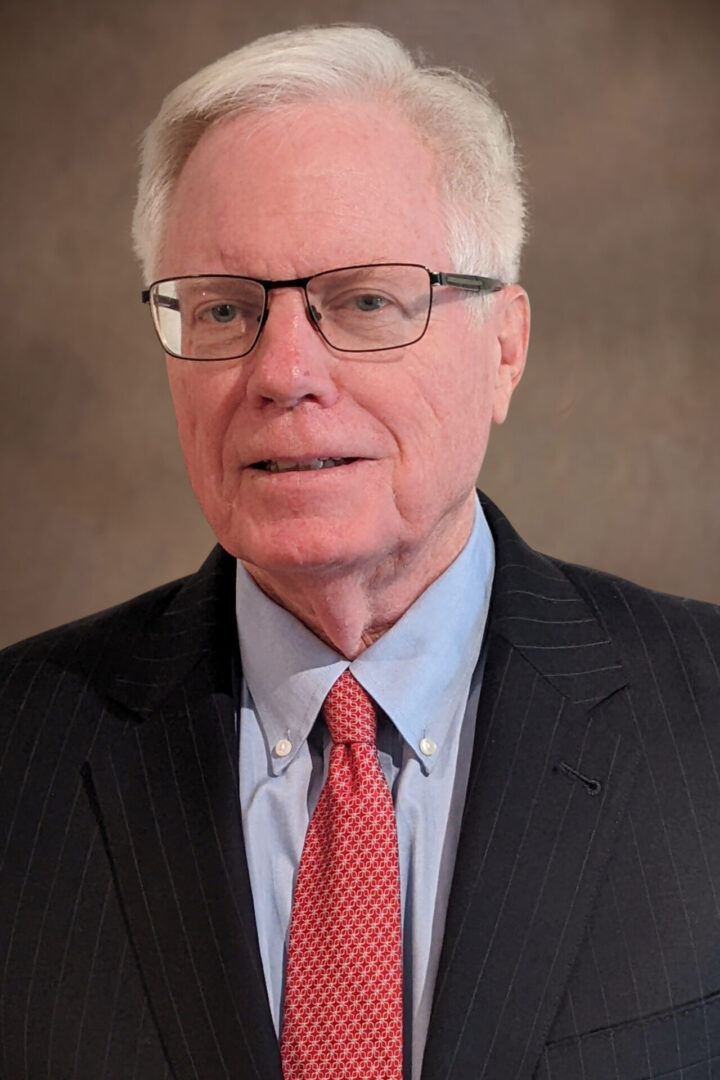 A picture of an old man with glasses wearing a black suit